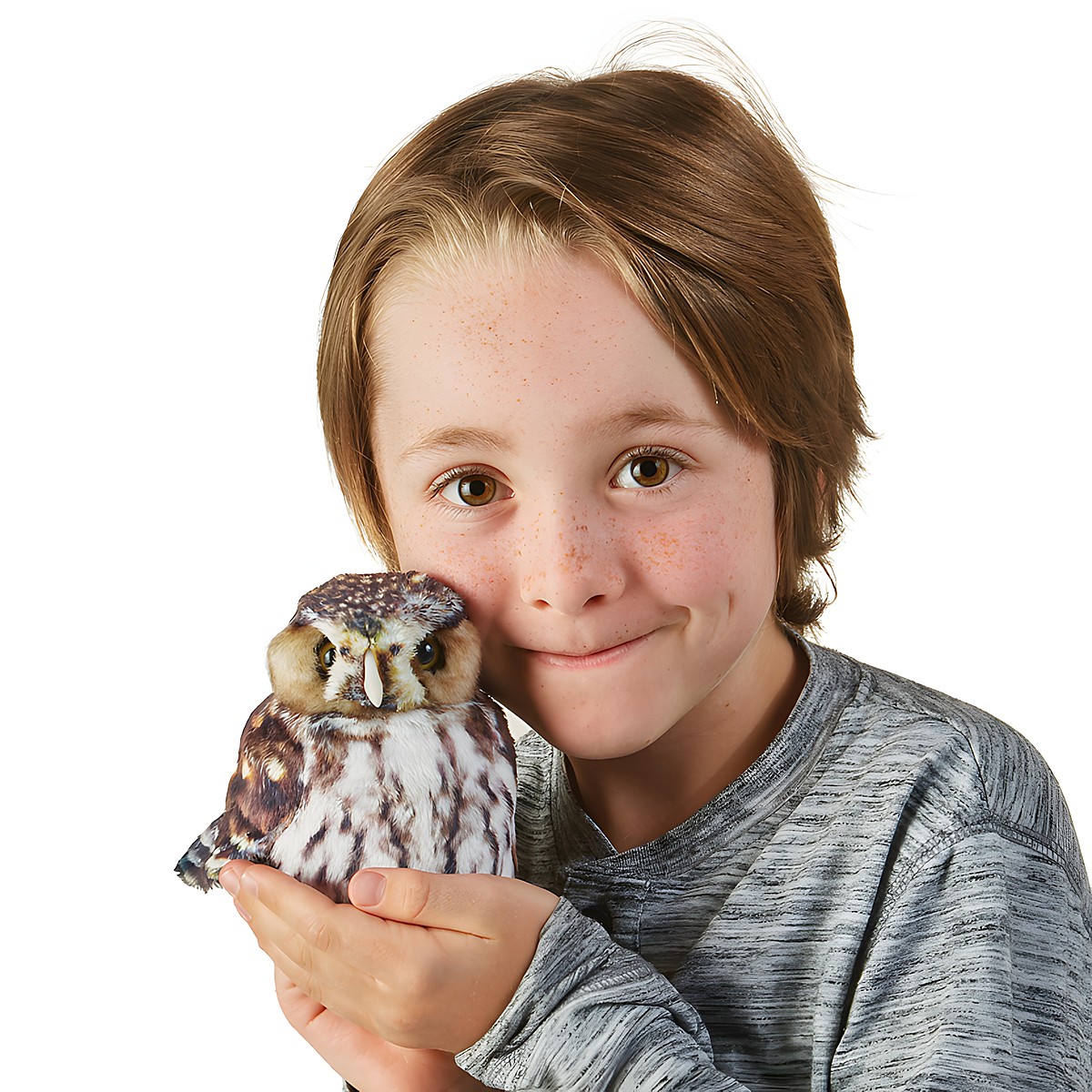 Child holding a Folkmanis pygmy owl hand puppet with brown-and-white plumage in their palm next to their face