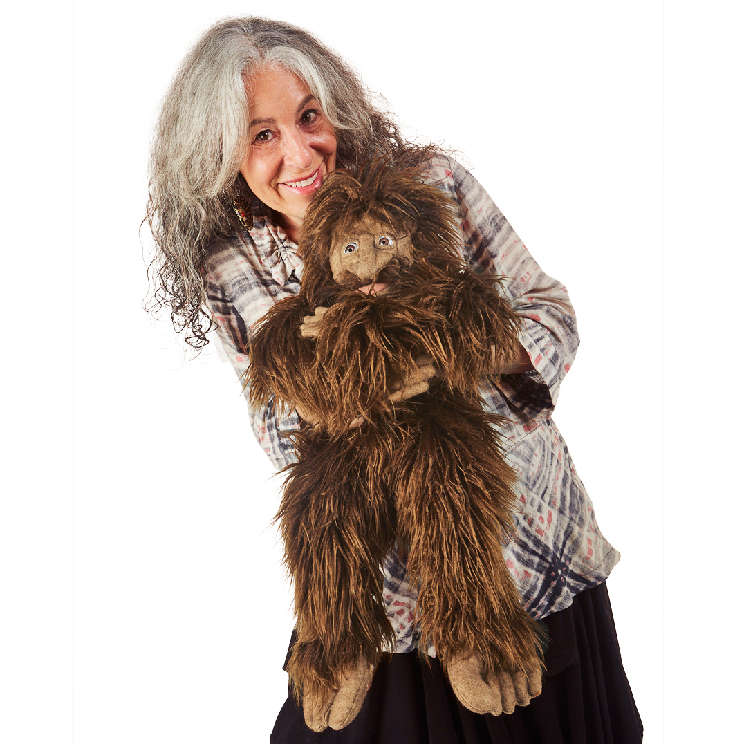 Folkmanis Handpuppe Bigfoot mit zottigem braunem Fell, von einer lächelnden Frau gehalten, Ganzkörperansicht vor weißem Hintergrund
