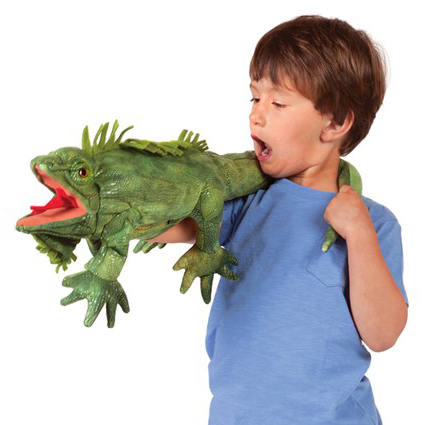 Boy operating a green Folkmanis iguana hand puppet with open mouth over his shoulder, side view