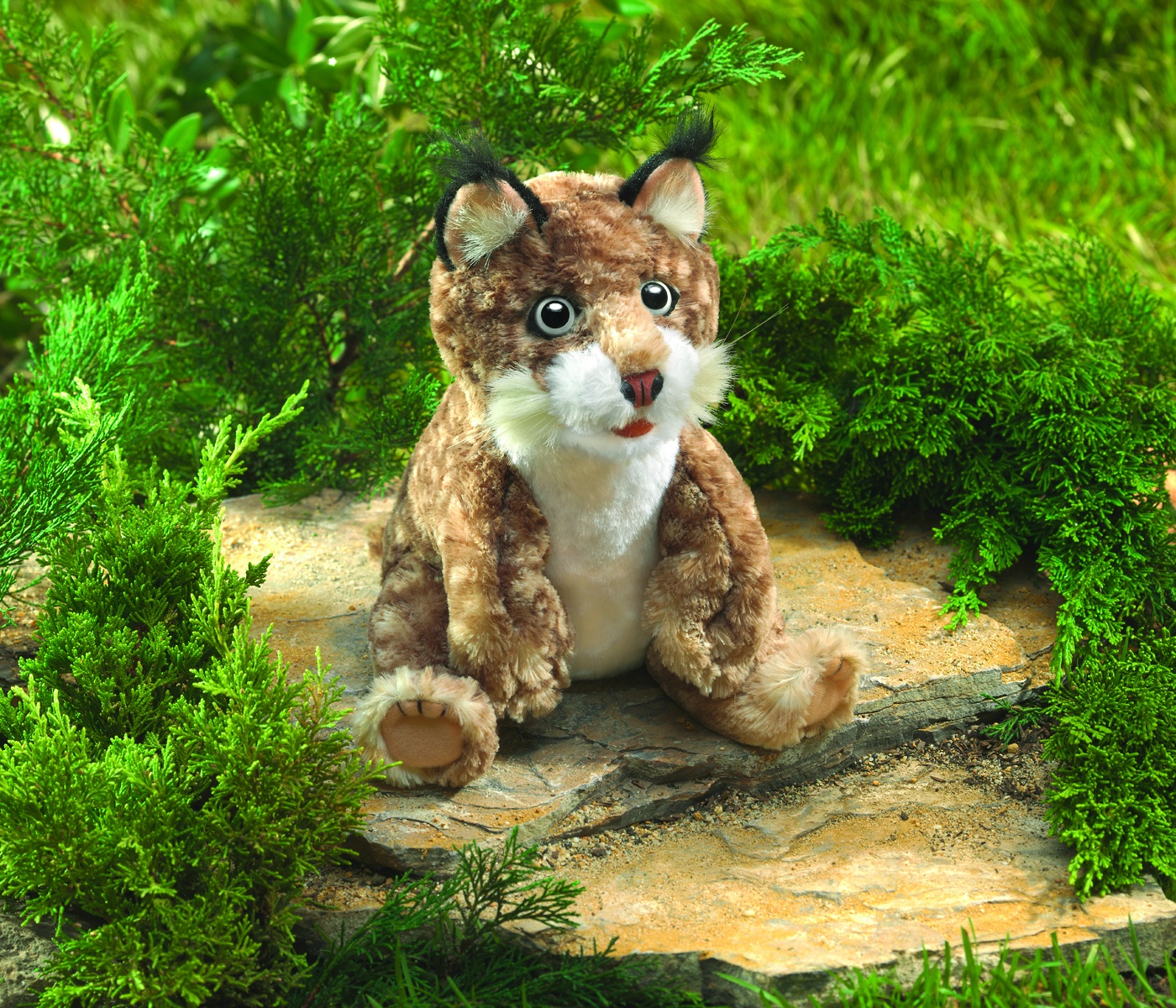 Folkmanis bobcat kitten hand puppet sitting on a stone, brown spotted fur, black ear tufts, white belly, open mouth