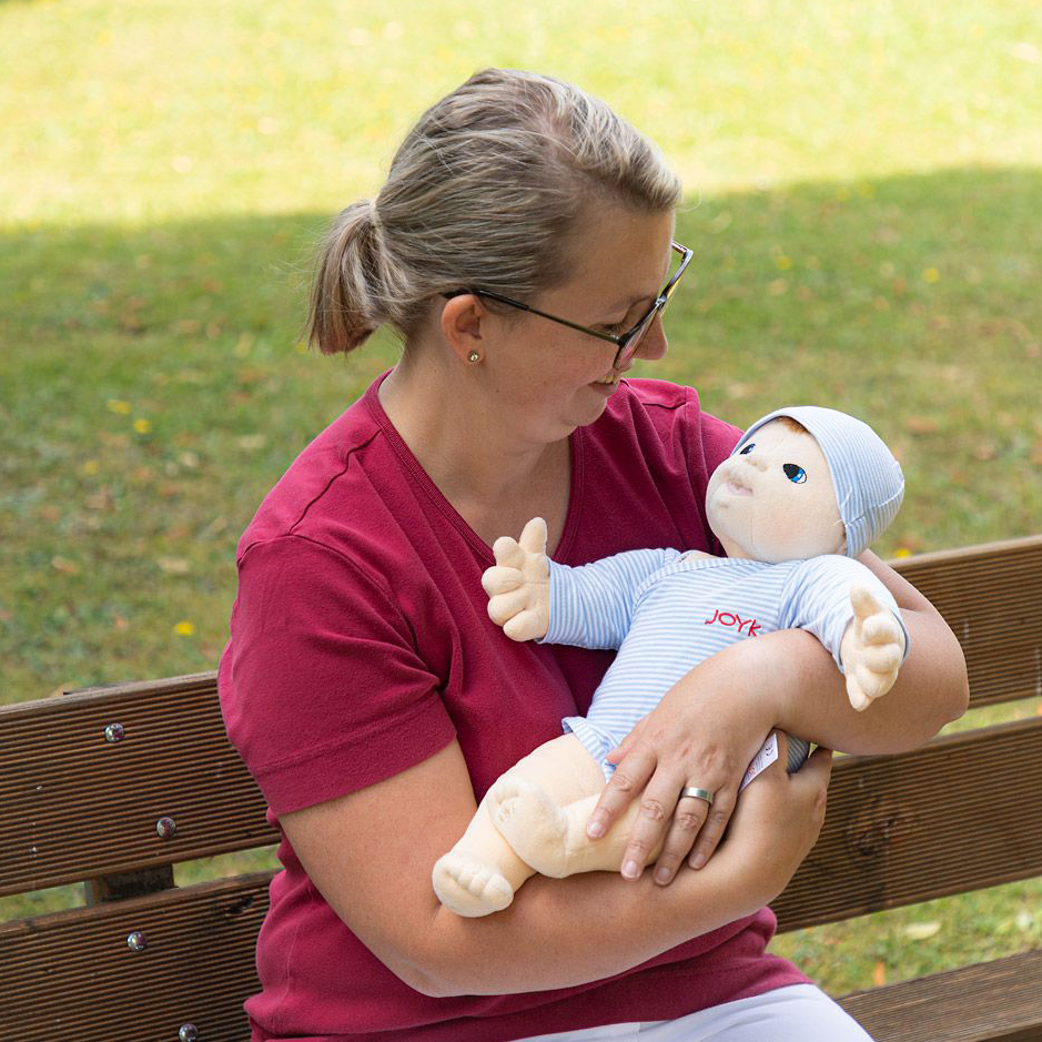 Frau hält die Joyk Empathiepuppe Baby Elias im Arm auf einer Parkbank
