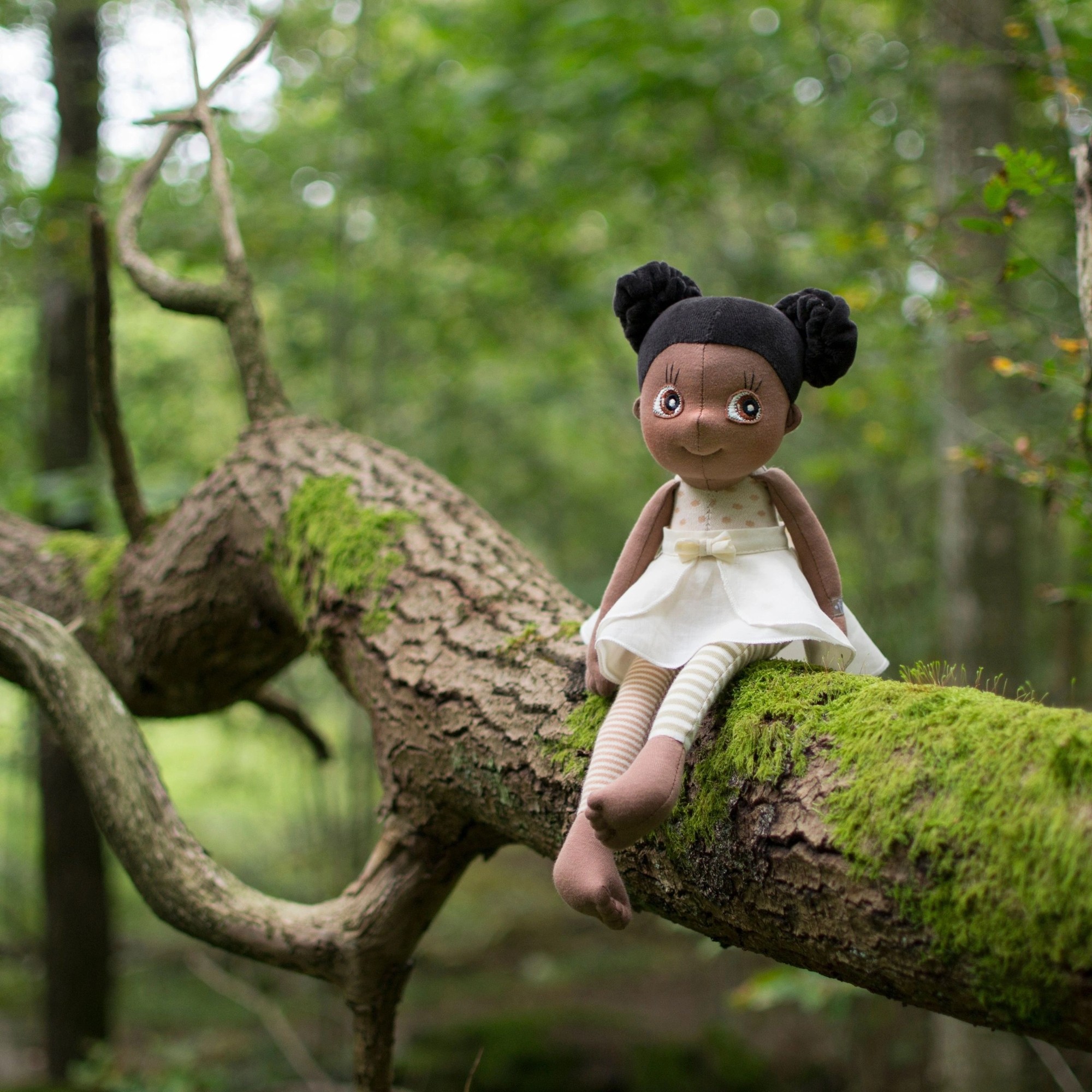 The Rubens EcoBuds doll Poppy sitting on a mossy tree trunk in the forest