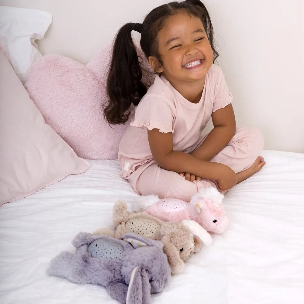 Cloud b Einschlafhilfe Dream Buddies, Gruppenfoto: lachendes Mädchen mit grauem, beigem und rosa Kuscheltier in Reihe