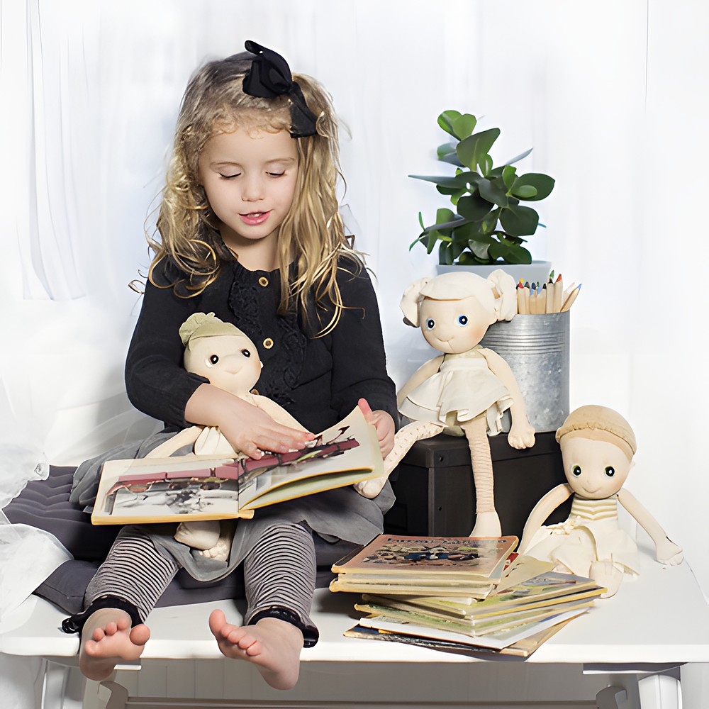 Child browsing picture books with the Rubens EcoBuds dolls, including Hazel