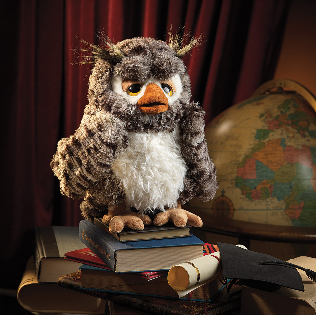 Folkmanis Handpuppe weise Eule mit braun-grauem Gefieder und weißem Bauch, sitzt auf Bücherstapel vor Globus