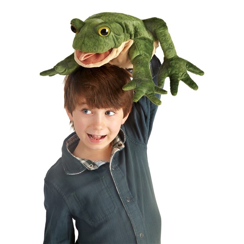 Lachender Junge hält Folkmanis Handpuppe Kröte mit geöffnetem Maul und grüner Strukturoberfläche über seinen Kopf.