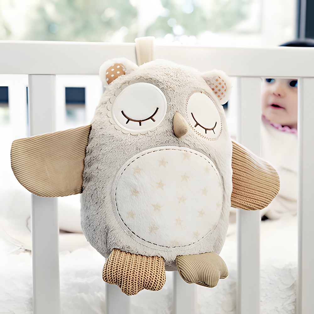 Cloud b Einschlafhilfe Nighty Night Owl, Anwendungsfoto: Eulen-Kuscheltier hängt am Gitterbett, Baby im Hintergrund
