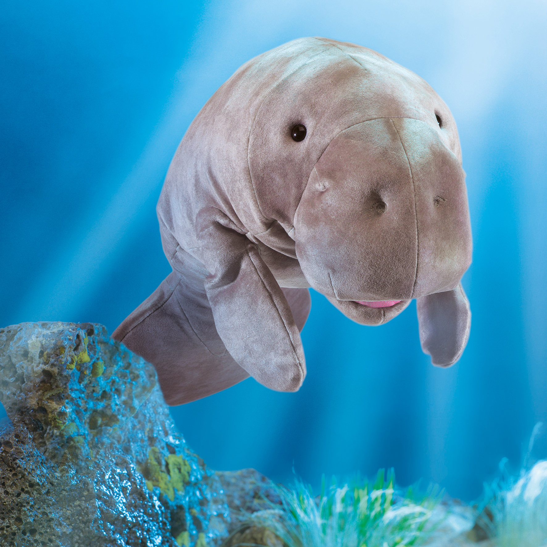 Folkmanis Handpuppe Seekuh aus grauem Plüsch mit beweglichem Maul, vor blauem Unterwasser-Hintergrund mit Felsen
