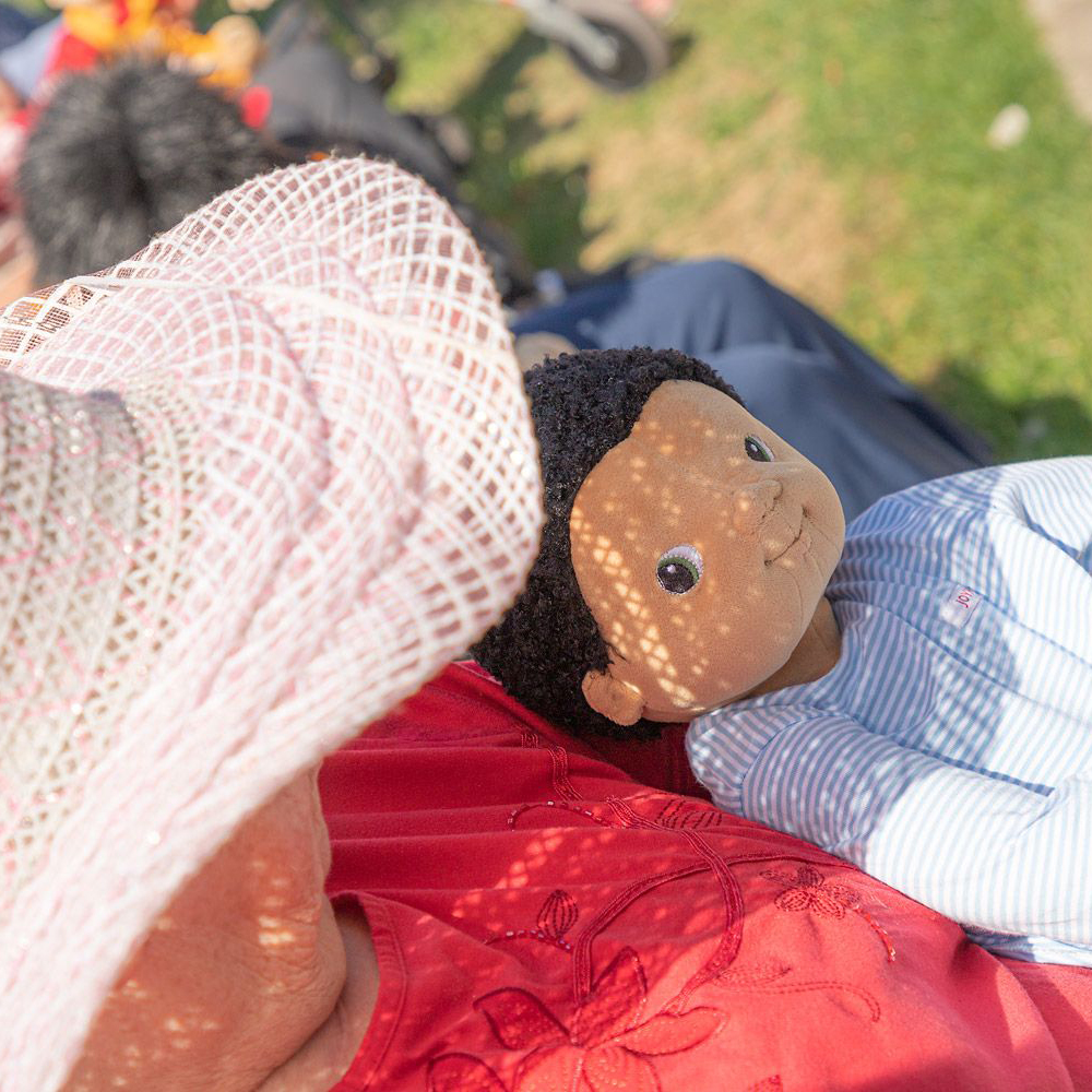 The Joyk empathy doll Antonio lying in the arms of a senior lady outdoors