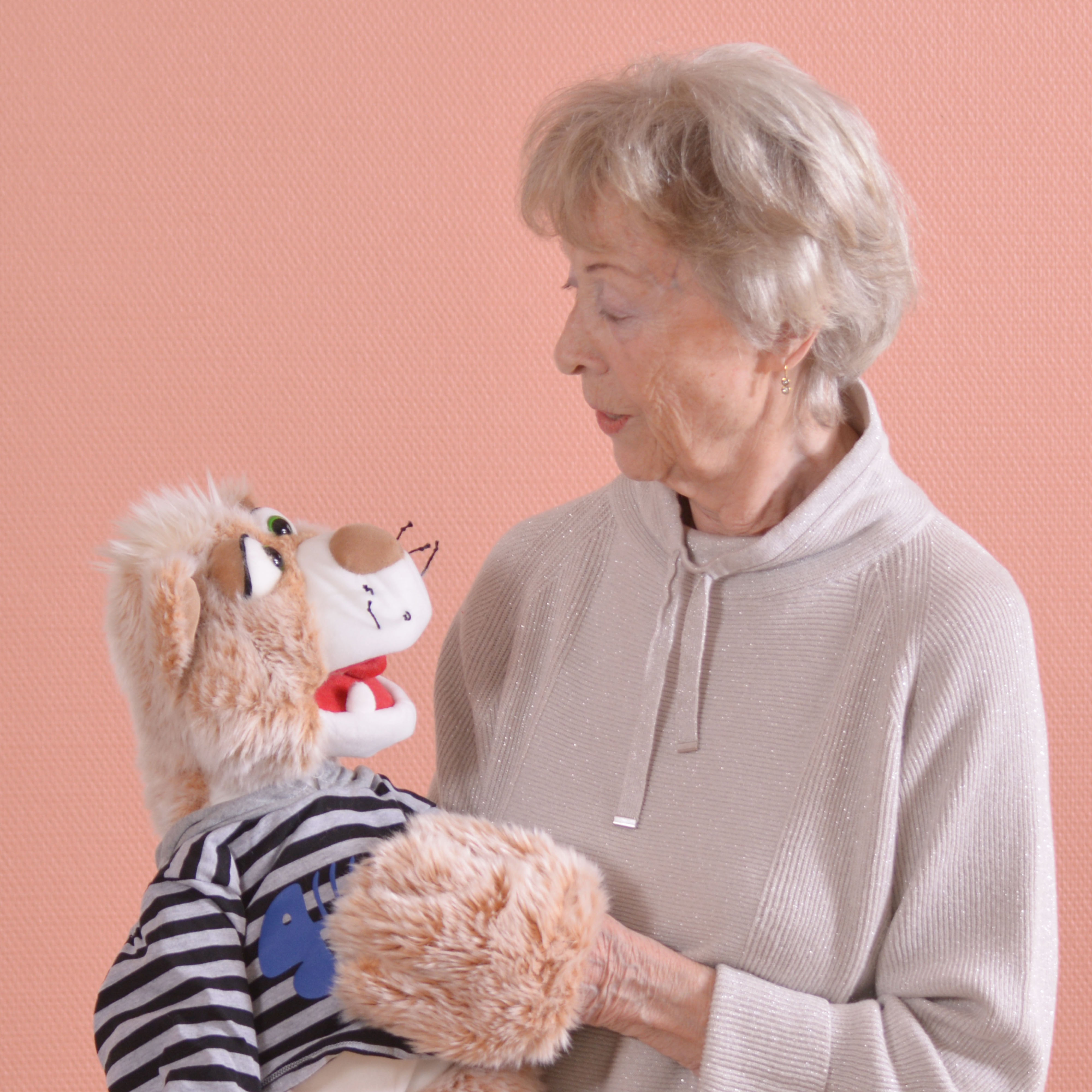 Elderly woman holding the Living Puppets hand puppet cat Wisky in the striped jumper, usage example