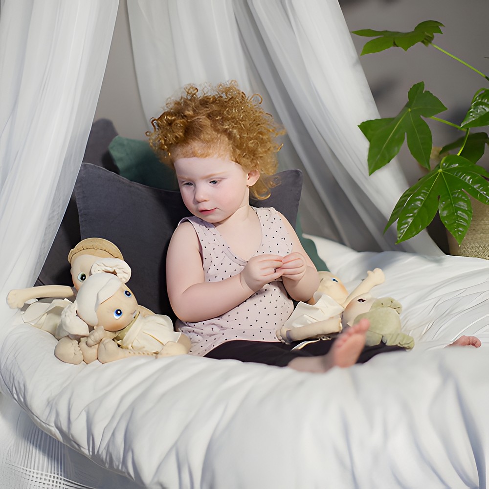 Child with the Rubens EcoBuds dolls, Hazel at their side, under the bed canopy