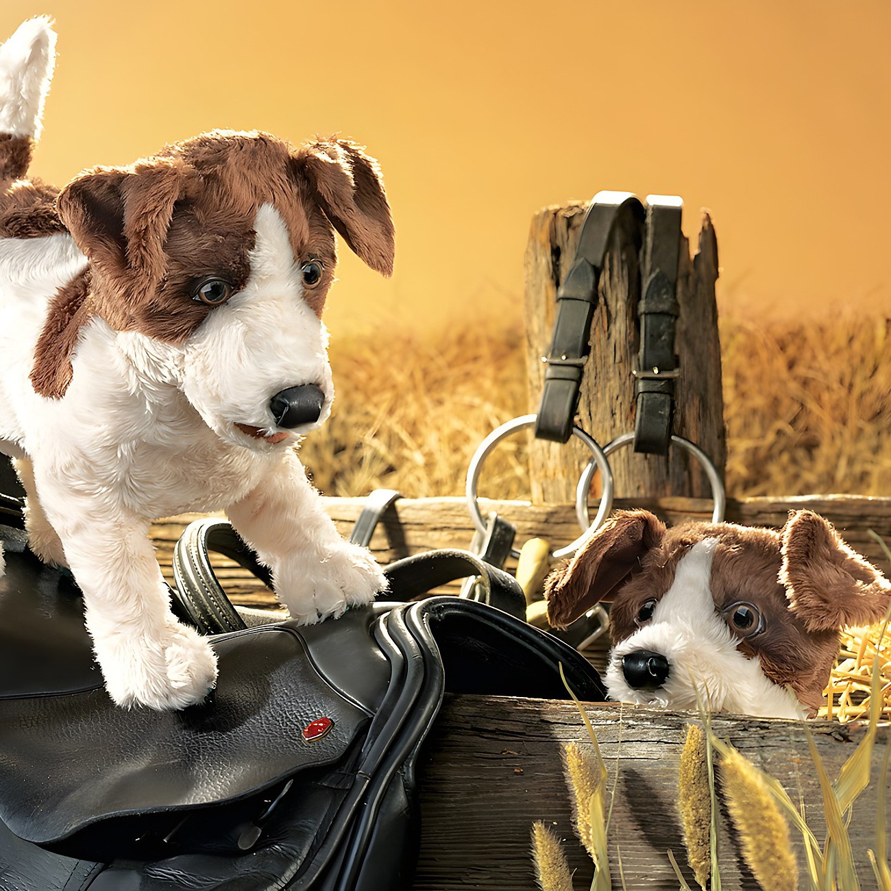 Two Folkmanis Jack Russell Terrier hand puppets in white and brown, one standing on a riding saddle, the other peeking out of a wooden crate filled with straw