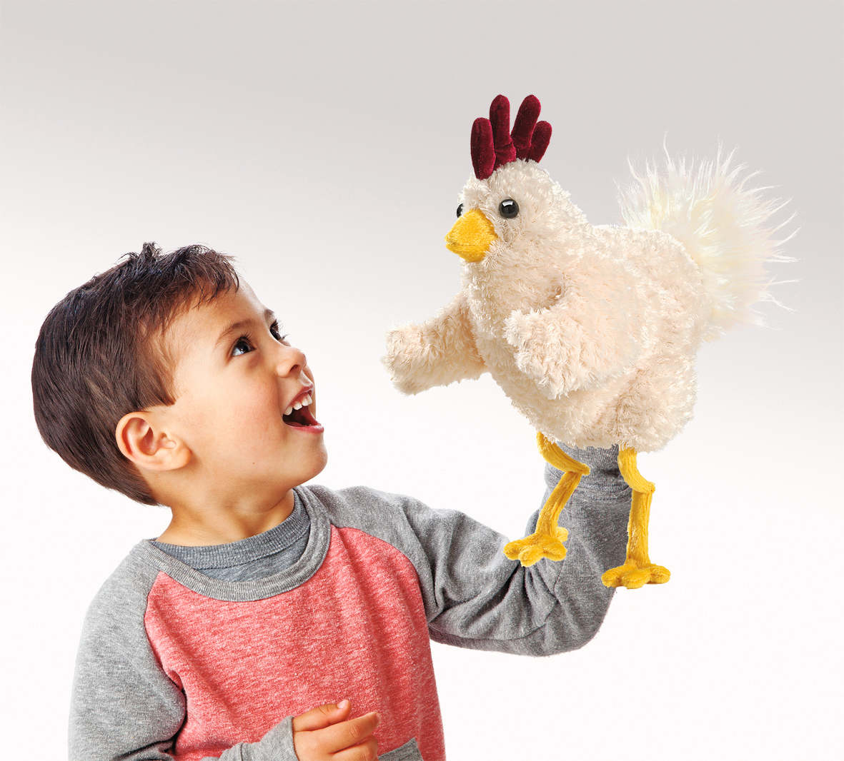 Boy playing with the Folkmanis Funky Chicken hand puppet featuring white plush, a dark red comb and yellow legs on his hand
