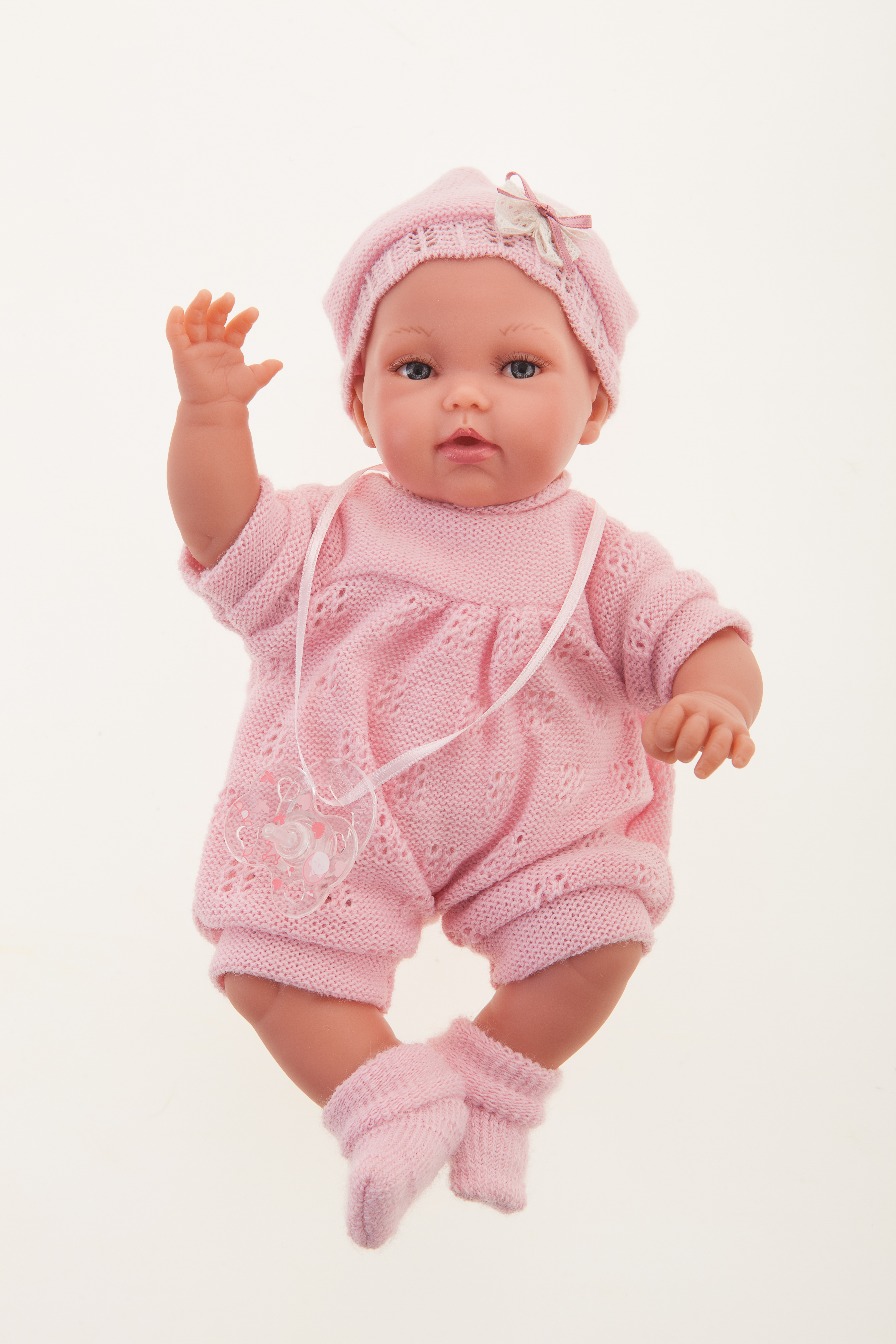 Antonio Juan Babypuppe Peke, realistische Puppe im rosa Strickoutfit mit Häkelmütze und Schleife, ein Arm erhoben, Frontalansicht