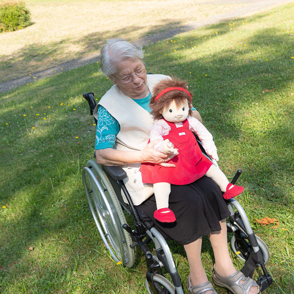 Seniorin im Rollstuhl mit der Joyk Empathiepuppe Ingrid auf dem Schoß