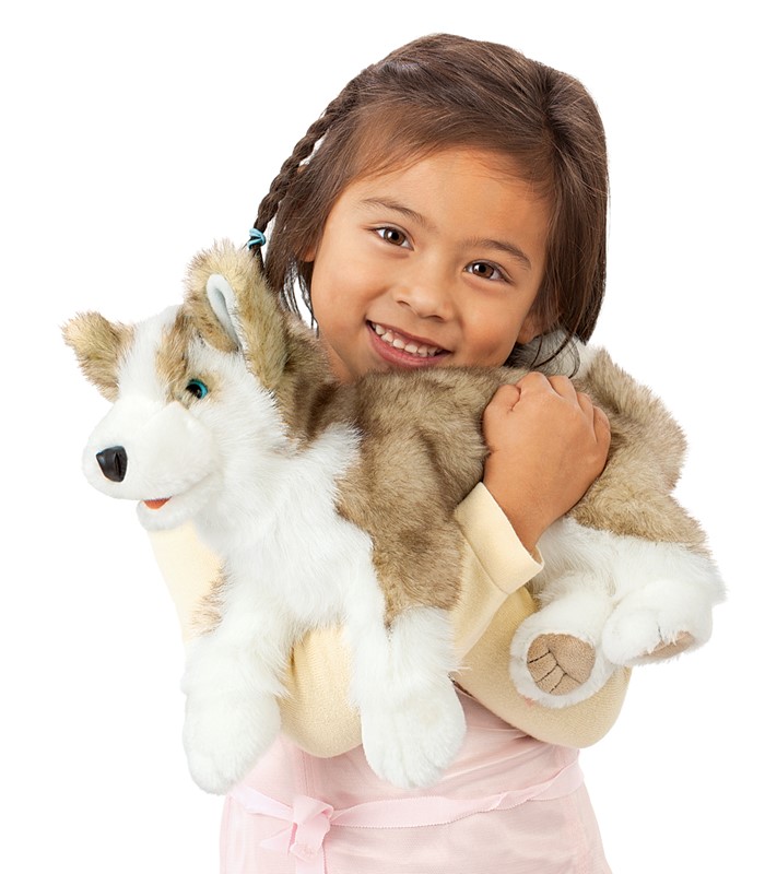 Mädchen hält Folkmanis Handpuppe Wolfsjunges mit grau-weißem Plüschfell und blauen Augen im Arm