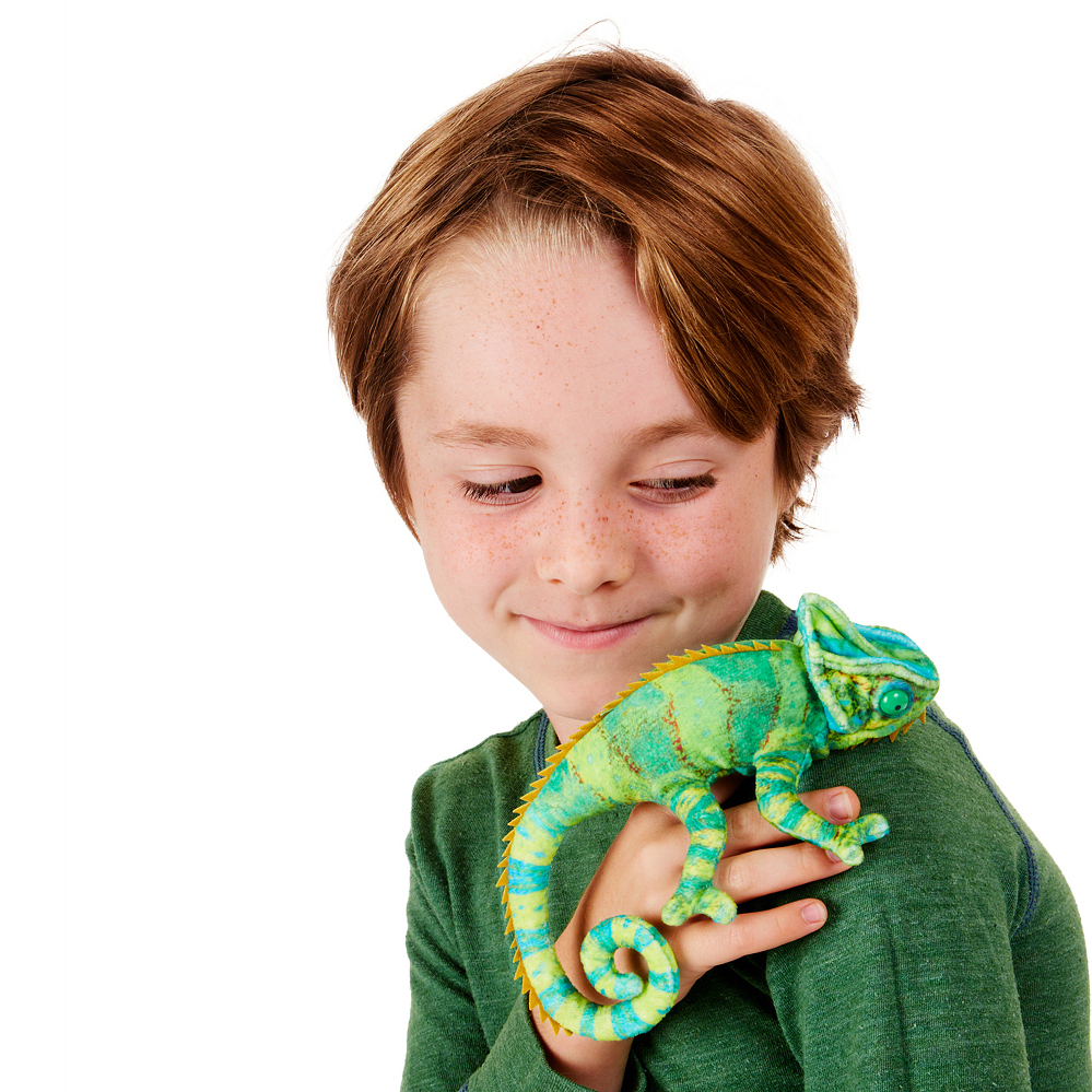 Boy holding a Folkmanis mini chameleon finger puppet in green and blue tones on his hand, smiling down at it