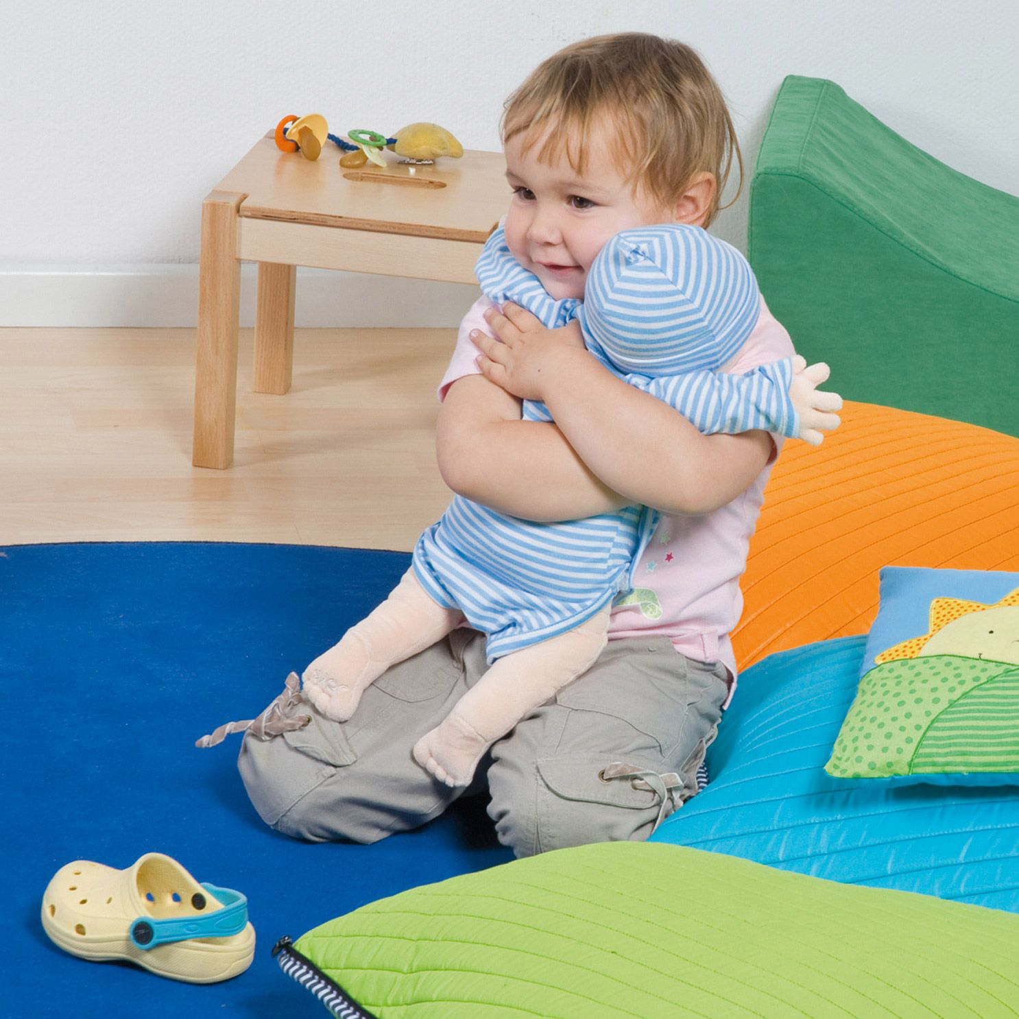 Kleinkind umarmt die Joyk Empathiepuppe Baby Elias auf einer Spielmatte
