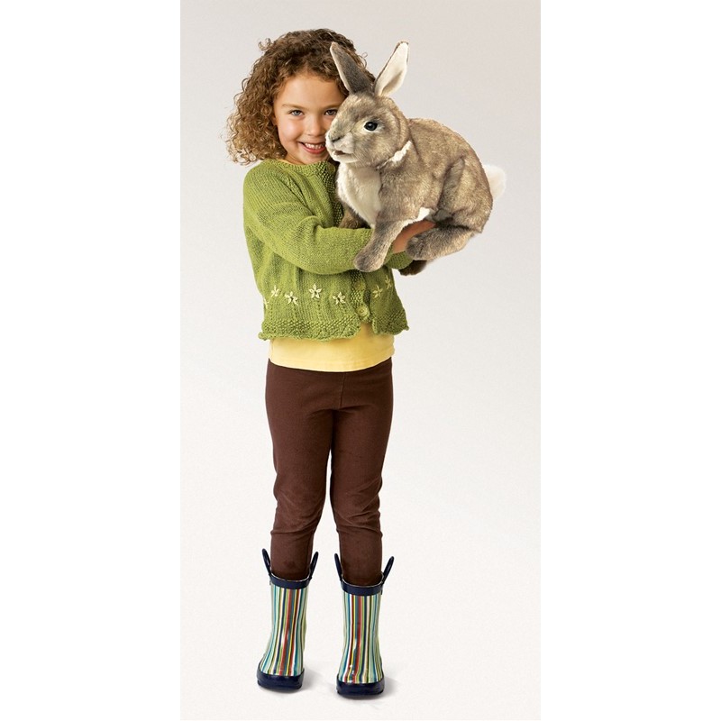 Mädchen hält die Folkmanis Handpuppe Baumwollschwanz-Kaninchen in graubraunem Plüsch auf dem Arm, Ganzkörperansicht.