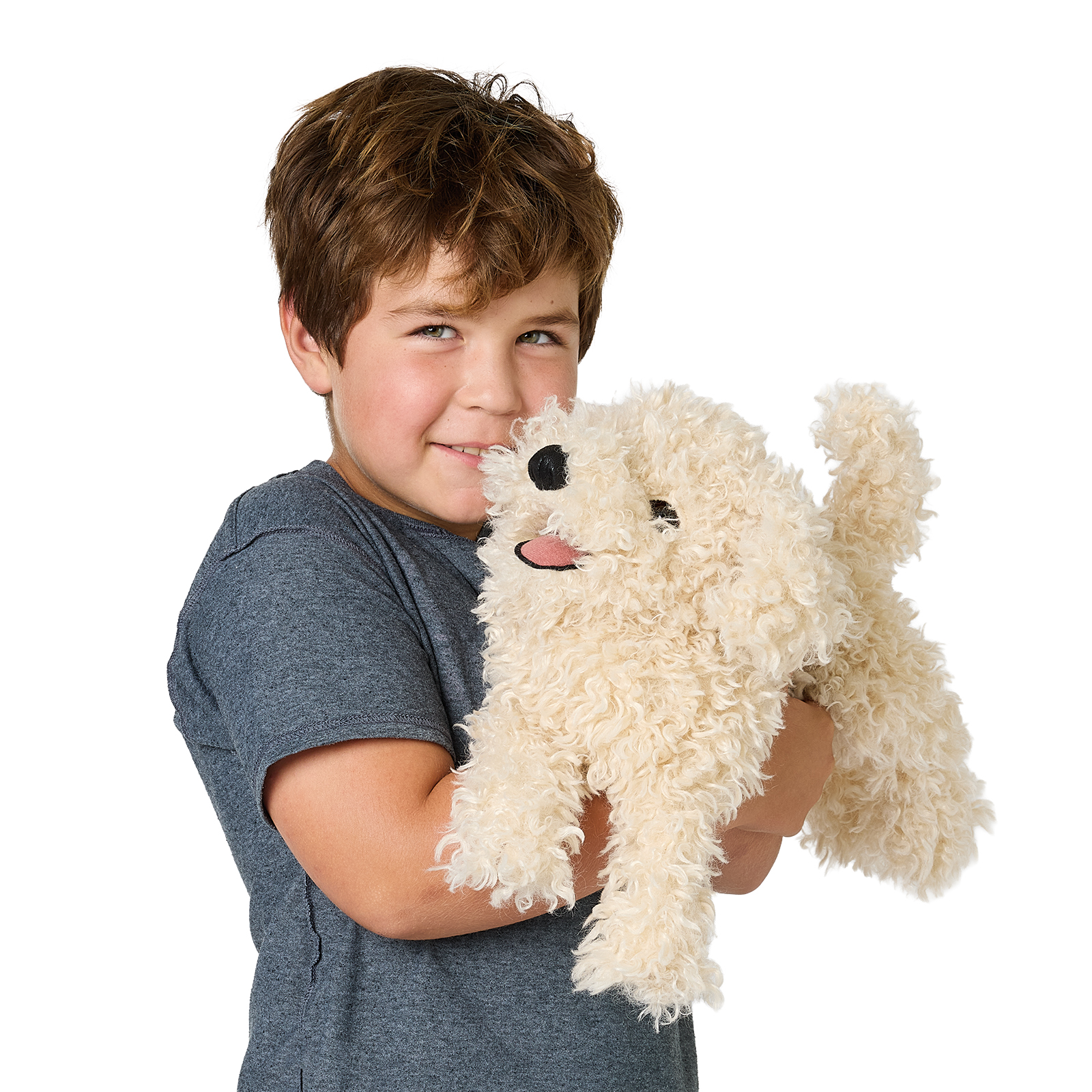 Lächelnder Junge hält die Folkmanis Handpuppe Pudelwelpe mit cremefarbenem Lockenfell und herausgestreckter Zunge vor weißem Hintergrund.