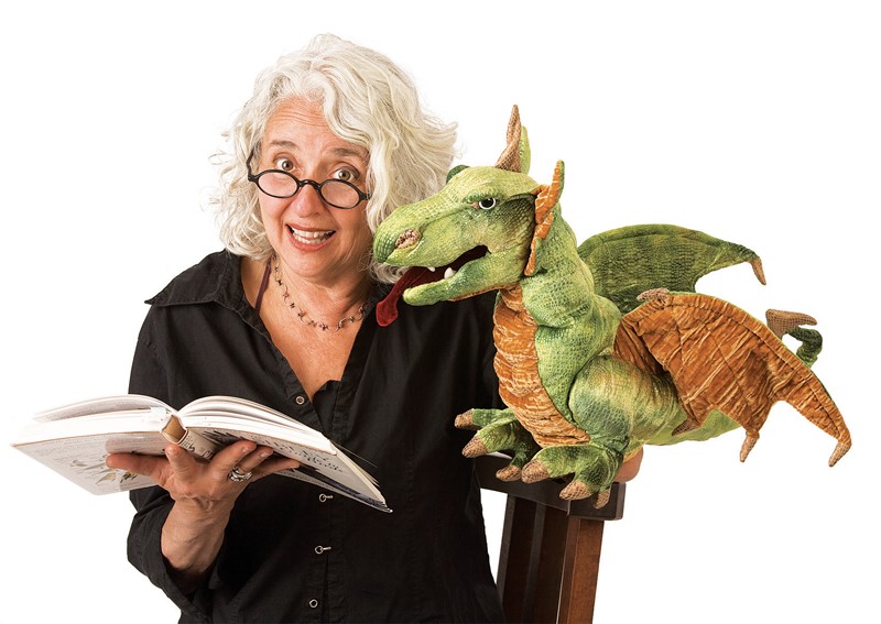 Folkmanis Handpuppe Lindwurm-Drache in Grün mit Flügeln, auf der Schulter einer Frau mit Buch sitzend