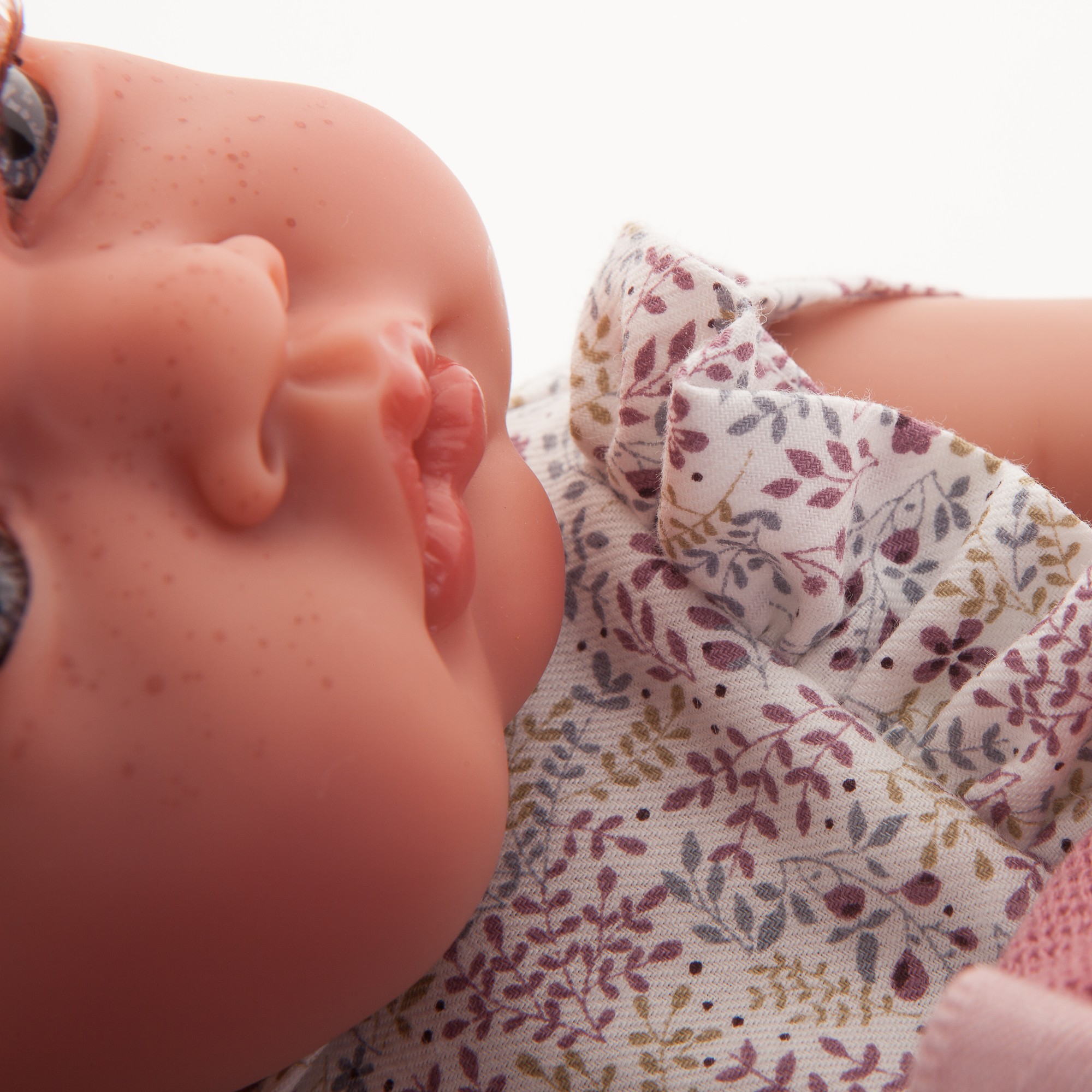 Antonio Juan baby doll New Born, close-up of the face turned to the side with floral dress and dusty pink knit sleeve