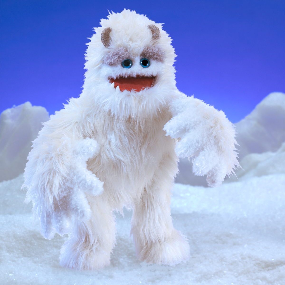 Folkmanis Handpuppe Yeti mit weißem Langfell, blauen Augen und geöffnetem Maul, vor winterlicher Schnee-Kulisse