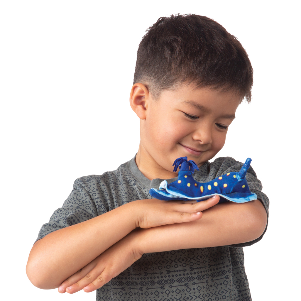 Junge hält lächelnd eine Folkmanis Fingerpuppe mini Ozeanschnecke in Blau mit gelben Flecken auf seinem Handrücken.