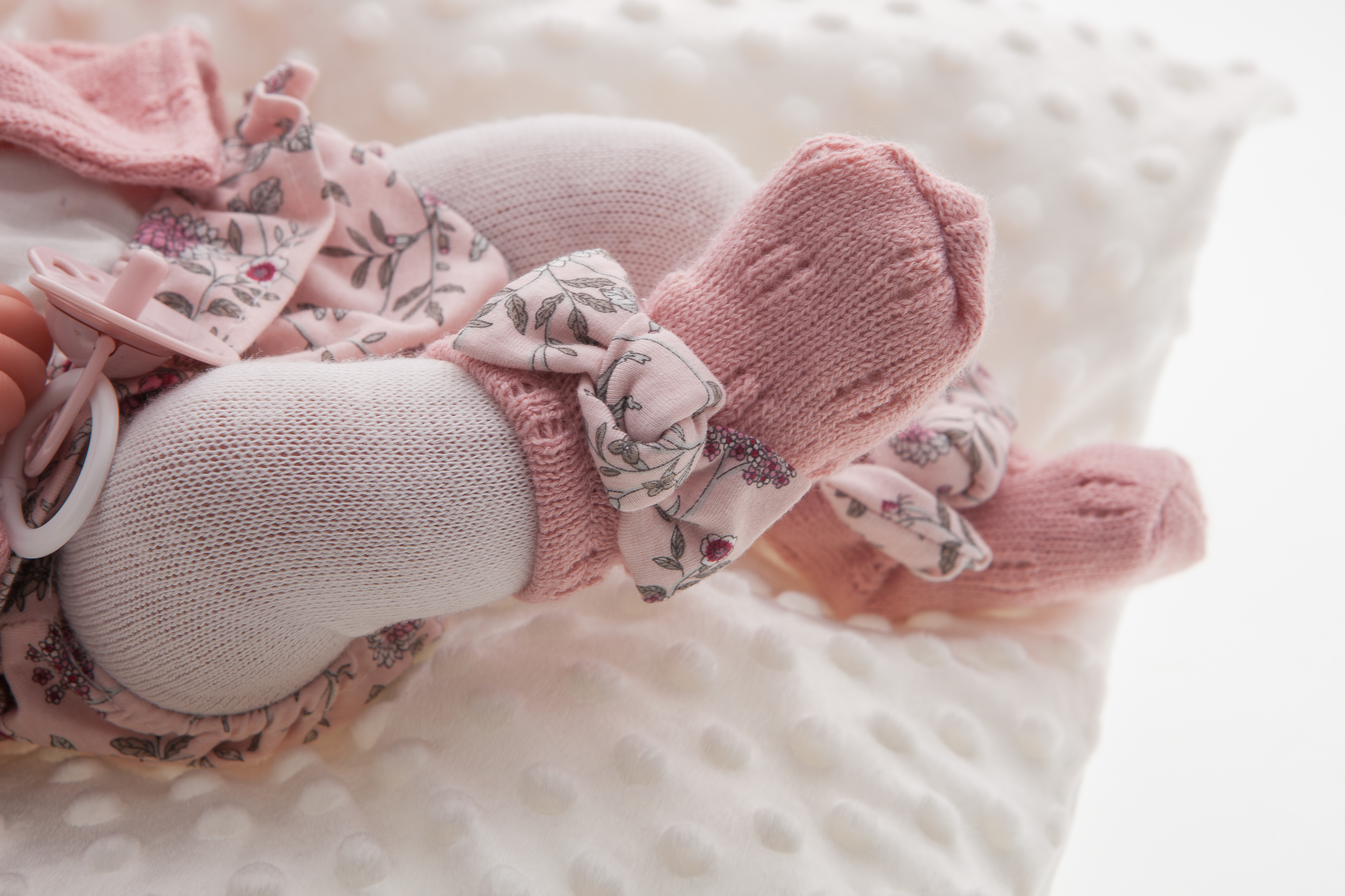 Antonio Juan Babypuppe Pipa, Detailaufnahme der Füßchen mit Blumenschleifen und rosa Strick-Söckchen auf weißem Kissen