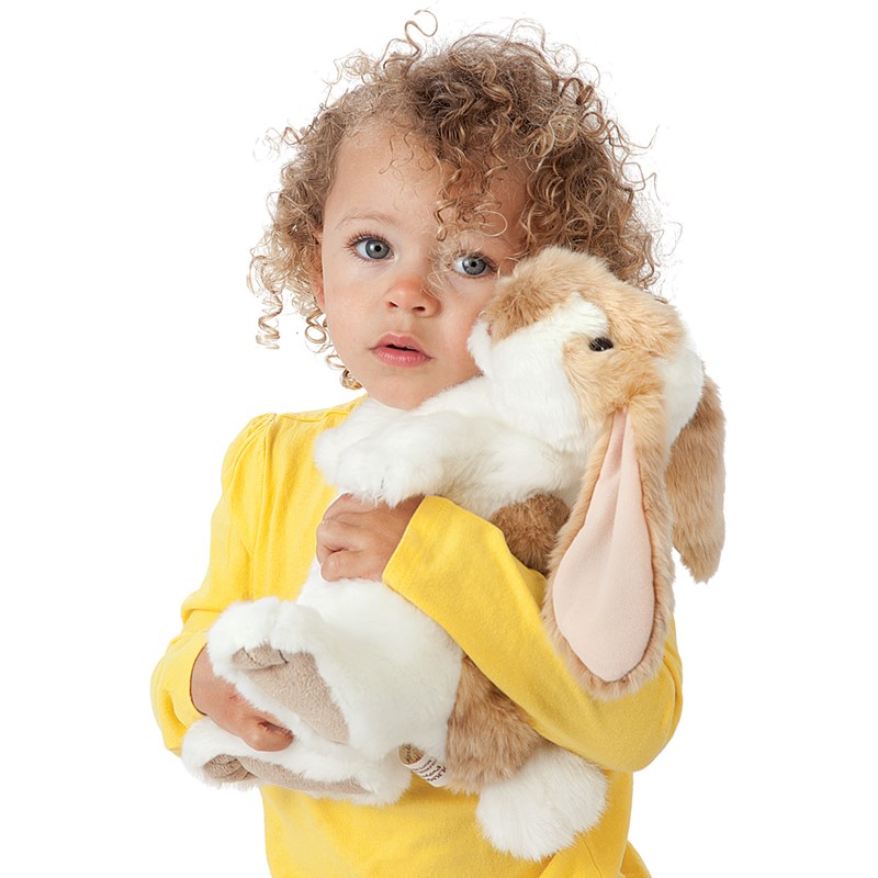 Kleines Mädchen hält Folkmanis Handpuppe stehendes Widderkaninchen mit beige-weißem Fell und langen Schlappohren im Arm.
