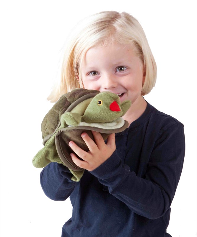 Smiling child holding the Folkmanis baby turtle hand puppet with a green head and red mouth in both hands