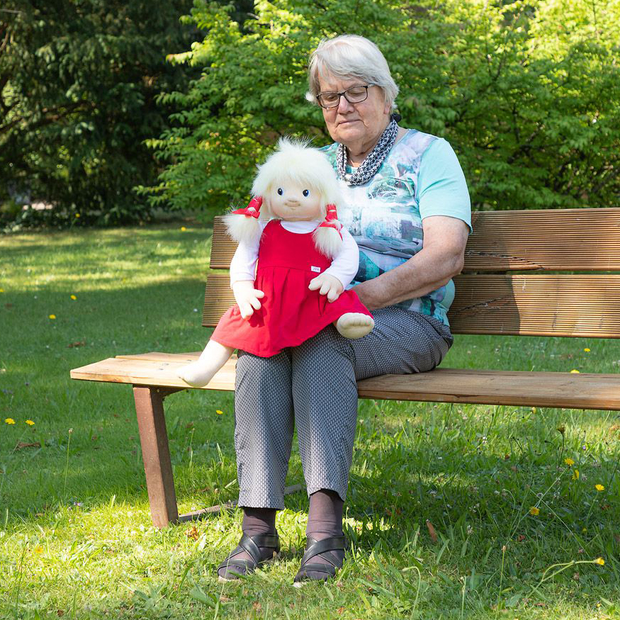Seniorin sitzt mit der Joyk Empathiepuppe Nelly auf einer Parkbank
